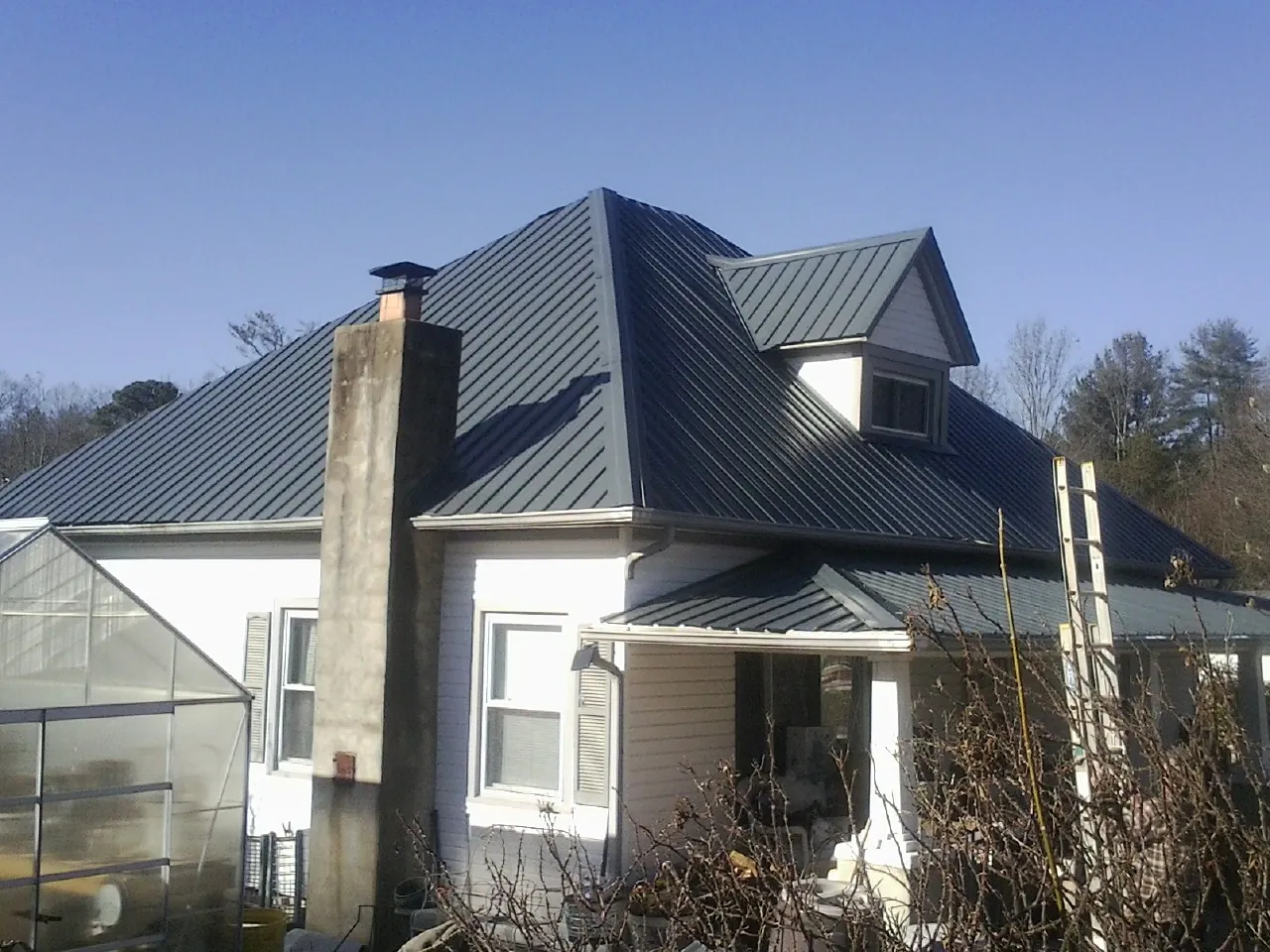 Dark blue standing seam metal roof on a white farmhouse with dormer — Slate & Tile Roof Repair by Roofing Brothers in Newcomb