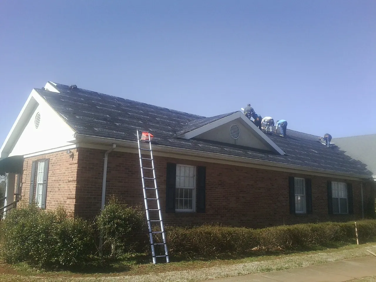 Crew tearing shingles off a brick ranch roof with a ladder set — Metal Roof Repair work by our crew in Newcomb