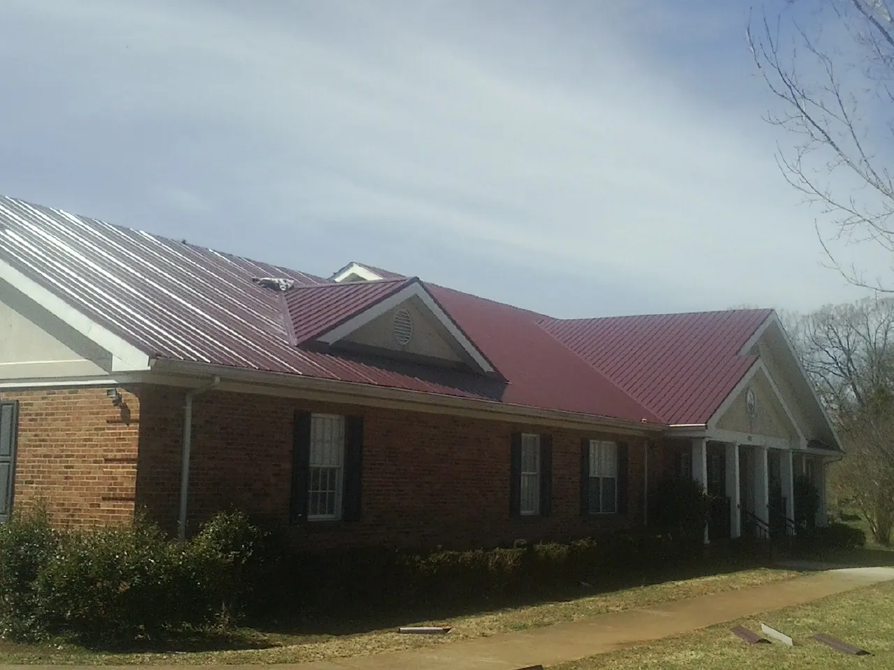 Red metal roof with gabled entries on a long brick building, from a Hail Damage Roof Repair job in Newcomb
