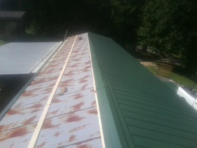 Old rusted panels beside newly installed green metal roofing — Wind Damage Roof Repair by Roofing Brothers in Newcomb