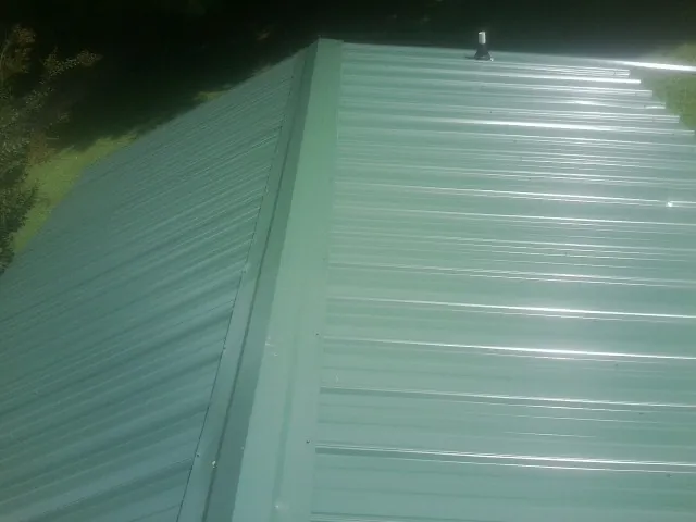 New green metal panels meeting at the ridge of a roof — Flat Roof Repair work by our crew in Newcomb