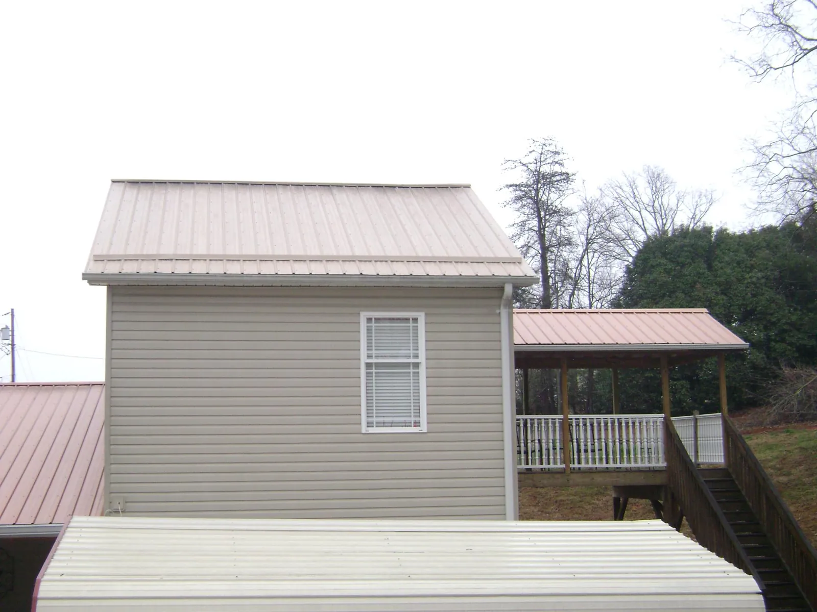 Tan metal roofs on a two story addition and attached porch, from a Roof Replacement job in Newcomb